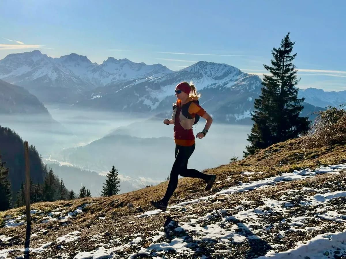 Trail runner on a snowy ridge with alpine panorama and morning mist